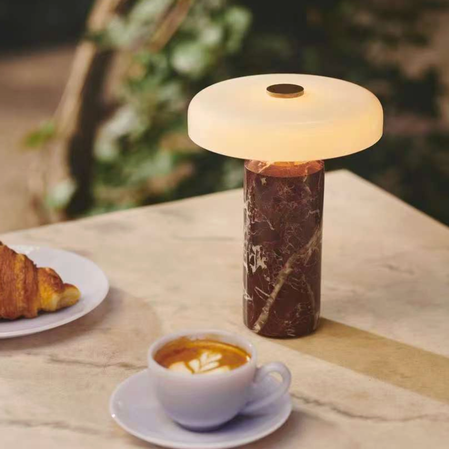Table lamp with marble base on a table with a cup of coffee and a croissant.