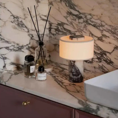 Decorative items on a marble countertop with a lamp and bottles.
